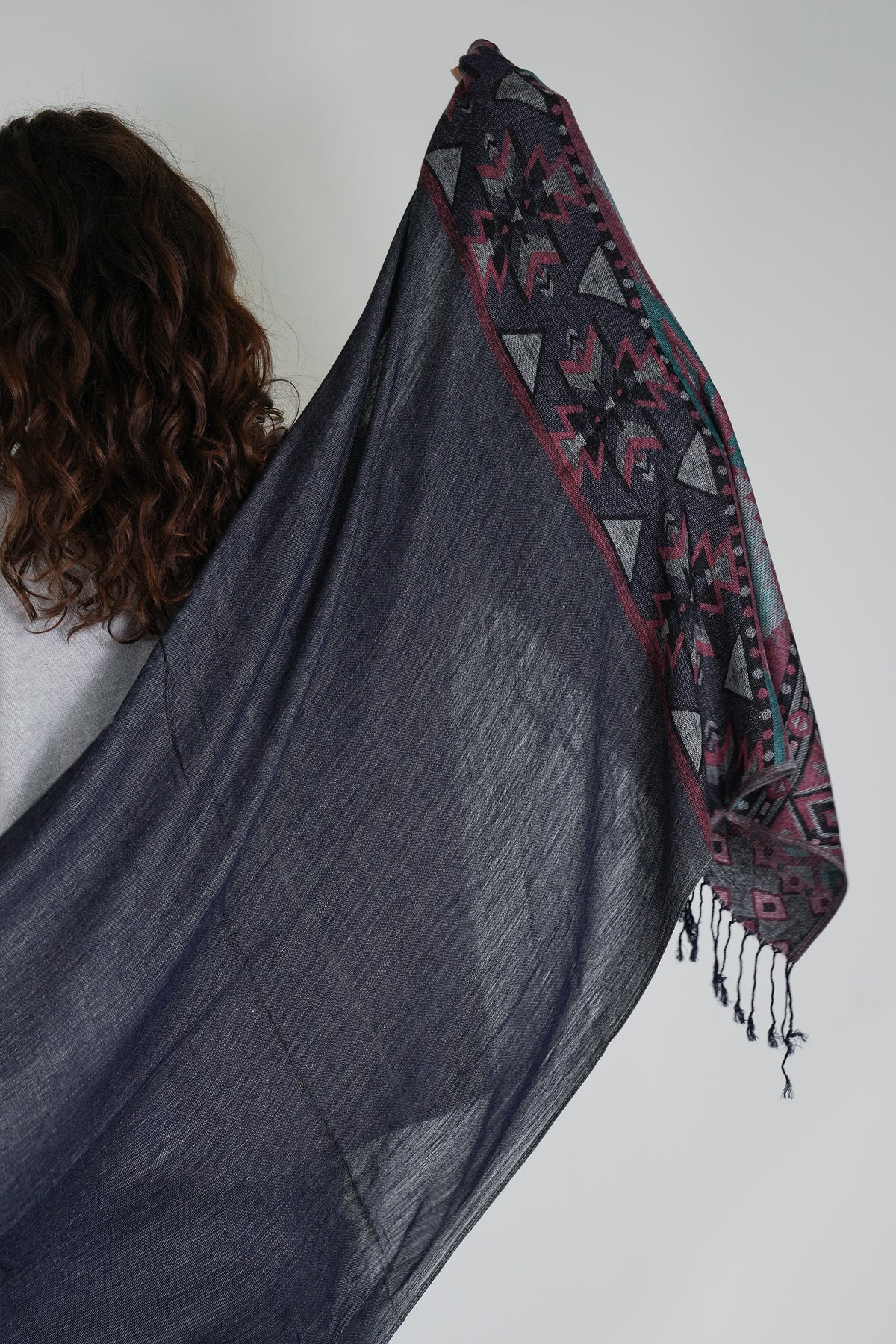 Person holding a dark gray shawl with a patterned edge against a white background