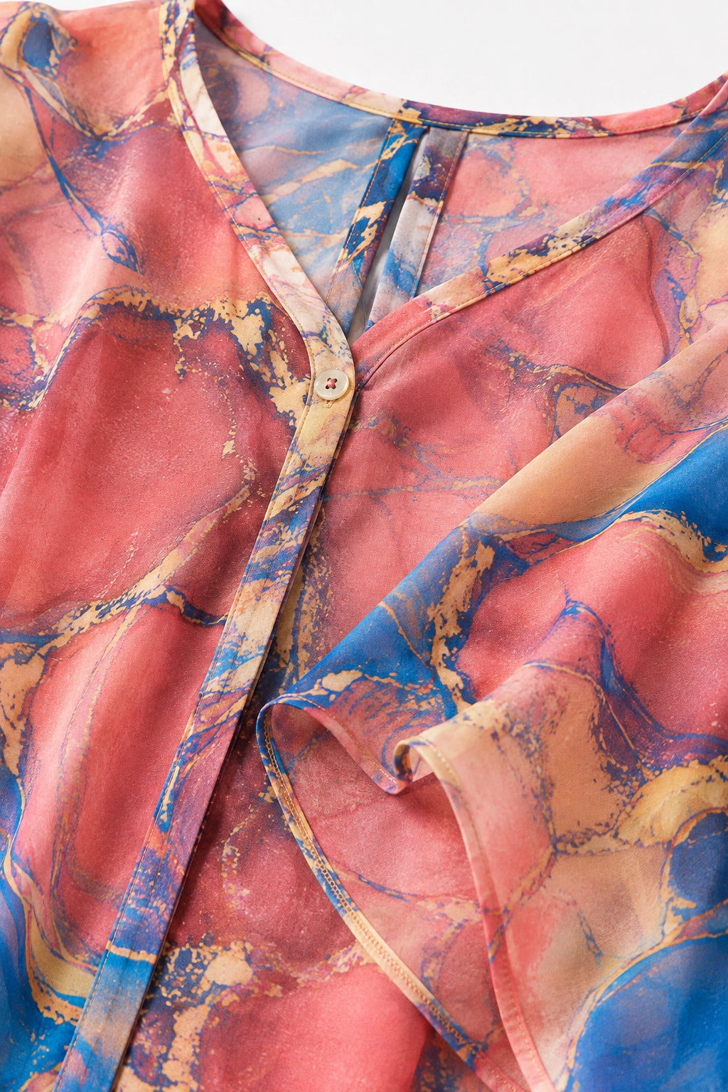 Close-up of a lightweight button-front top with a soft abstract marble print in pink, blue, peach, and gold tones.