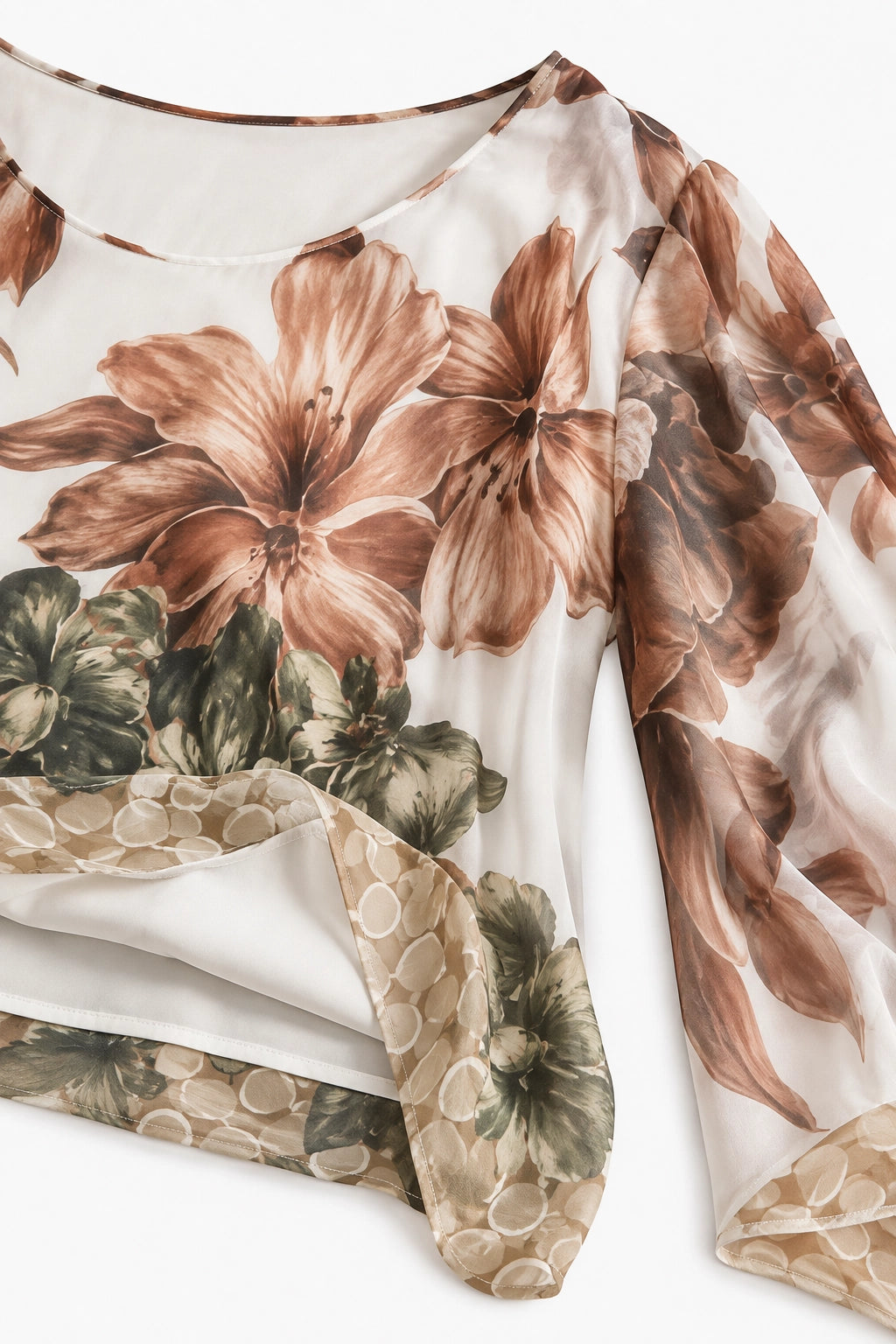 A close-up of a long-sleeve blouse with a large floral print in brown and olive green on a white base, featuring a draped hemline with a textured beige pattern.