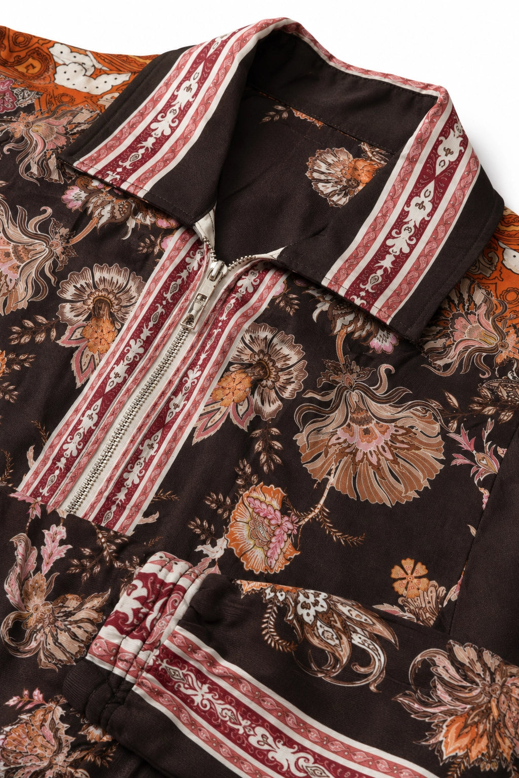 A close-up of a patterned jacket or overshirt featuring a dark brown base with a floral and paisley print in rust, beige, and orange, accented by striped collar and placket details.