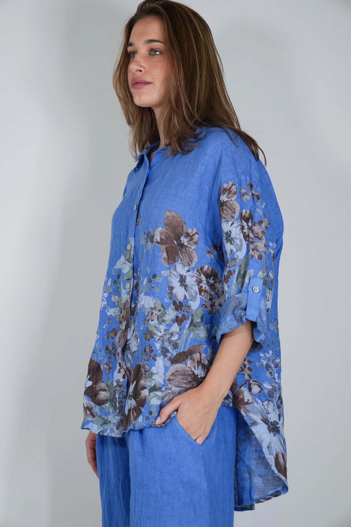 A woman wearing a blue button-up shirt with a brown and gray floral print, paired with matching blue pants, photographed against a plain light gray background.