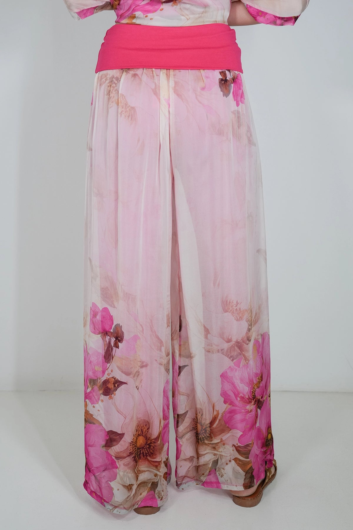 Pink wide-leg chiffon pants with a floral print and a matching pink waistband, shown on a model from the back against a white studio background.