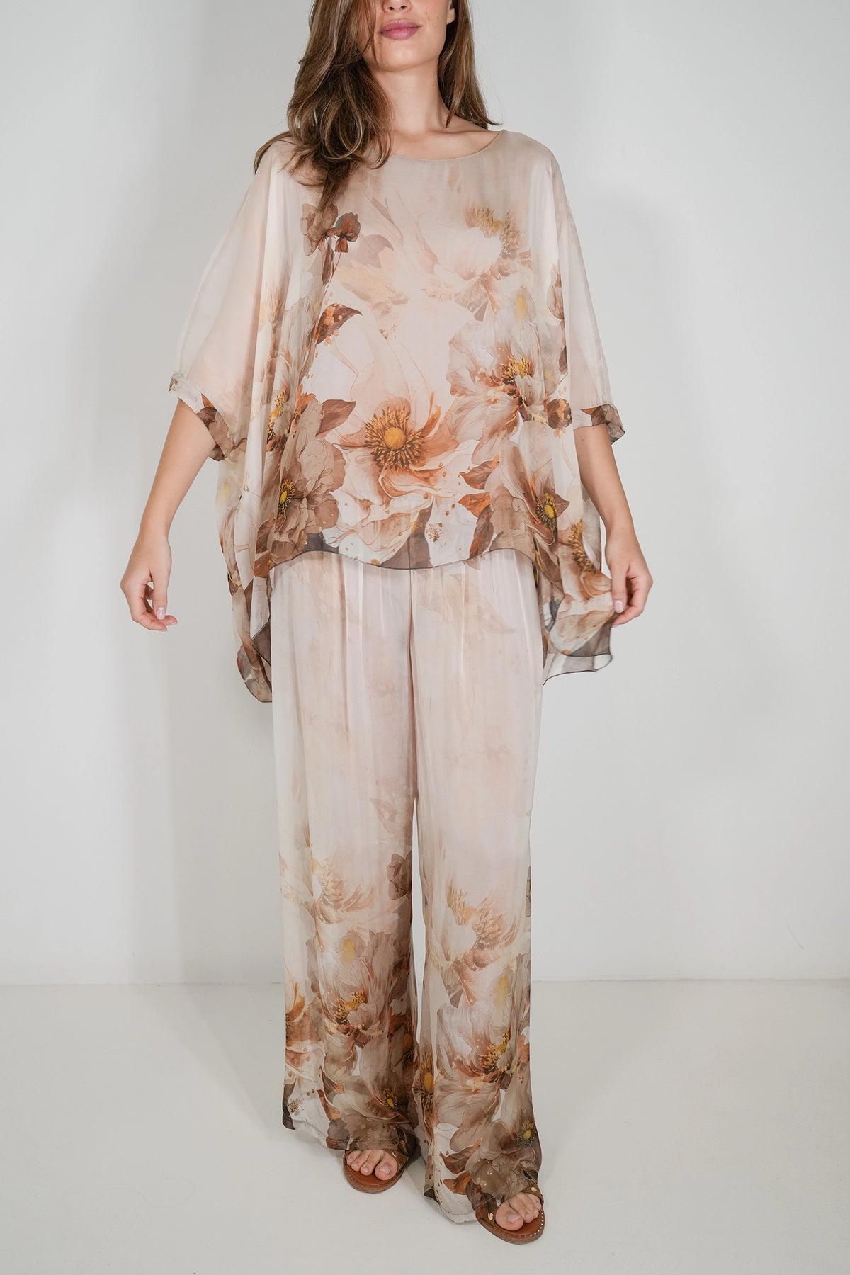 A woman modeling a sheer, lightweight two-piece set with a soft beige base and a brown and muted orange floral print, consisting of a loose short-sleeve top and matching wide-leg pants.