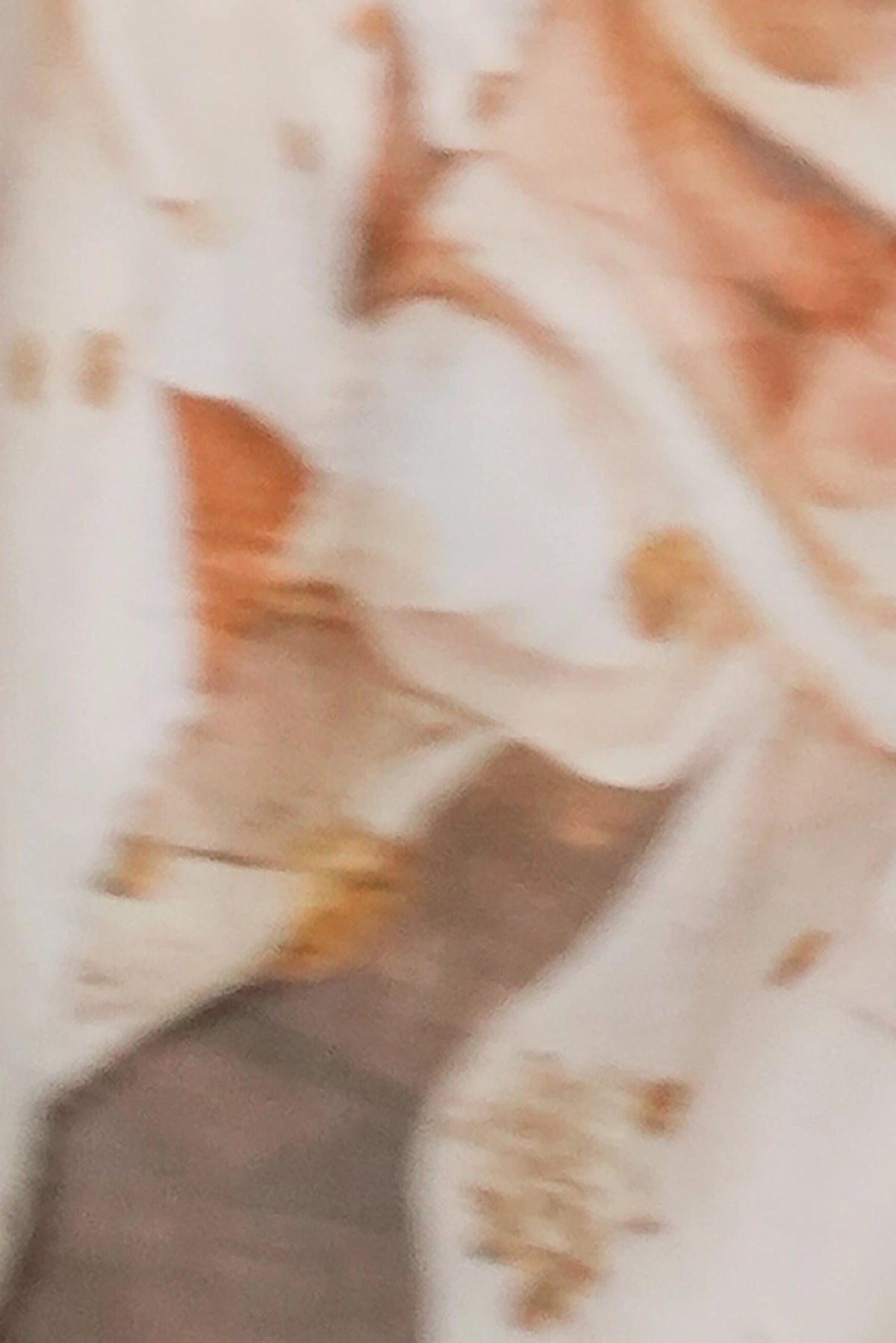 A close-up, blurry view of a white or cream fabric with warm brown and orange floral or abstract printed details.