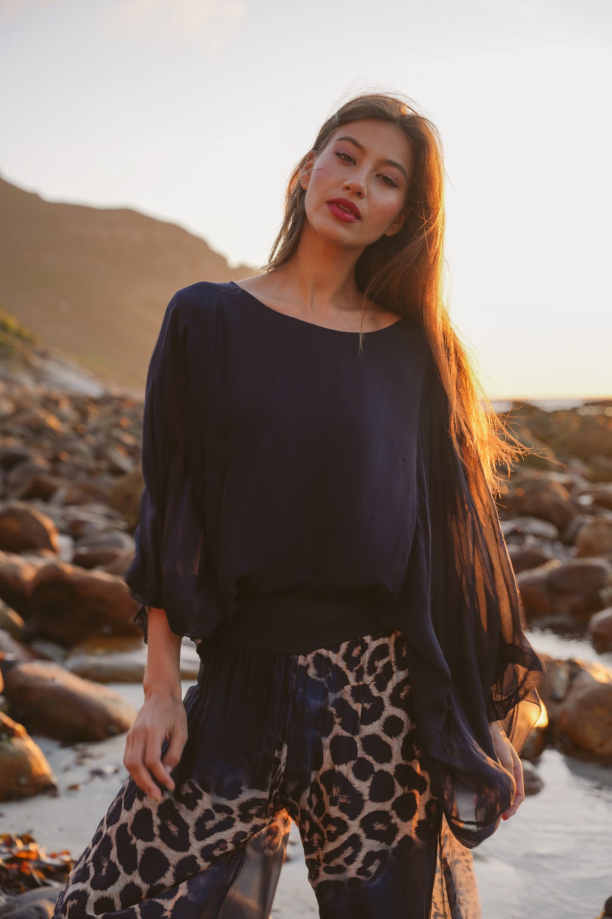 Woman standing on a rocky beach with mountains in the background
