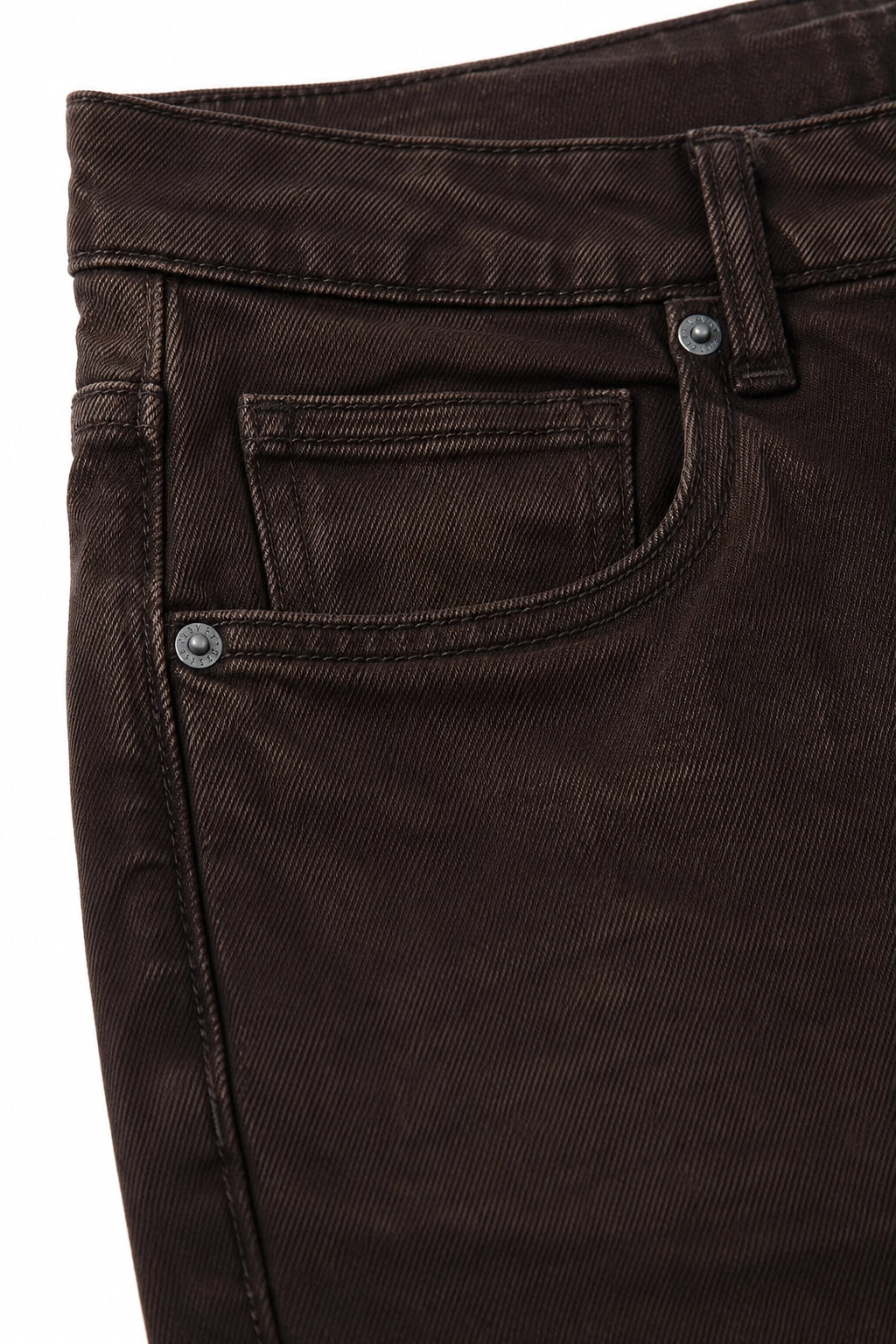 Close-up of dark brown denim jeans showing the front pocket, waistband, and metal rivets against a white background.
