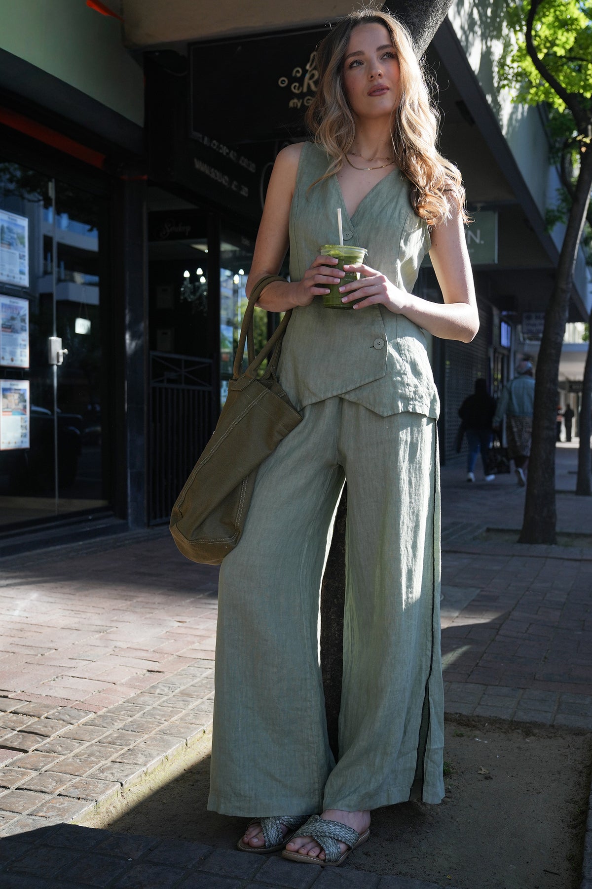 Woman in a green outfit holding a drink on a city street