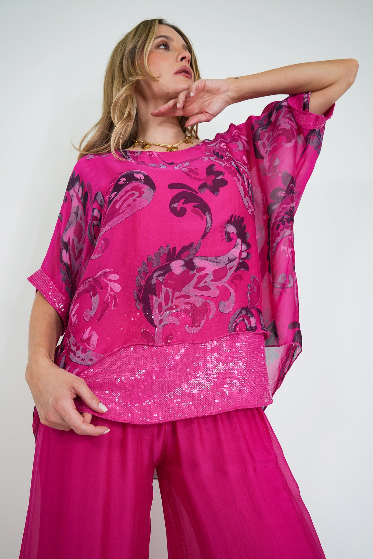 Woman wearing a bright pink top with black floral patterns and matching pink pants on a white background