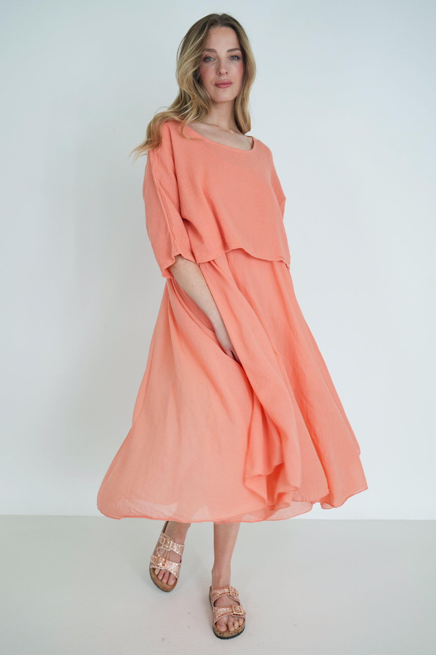 Woman wearing a peach-colored dress with a slit on a white background