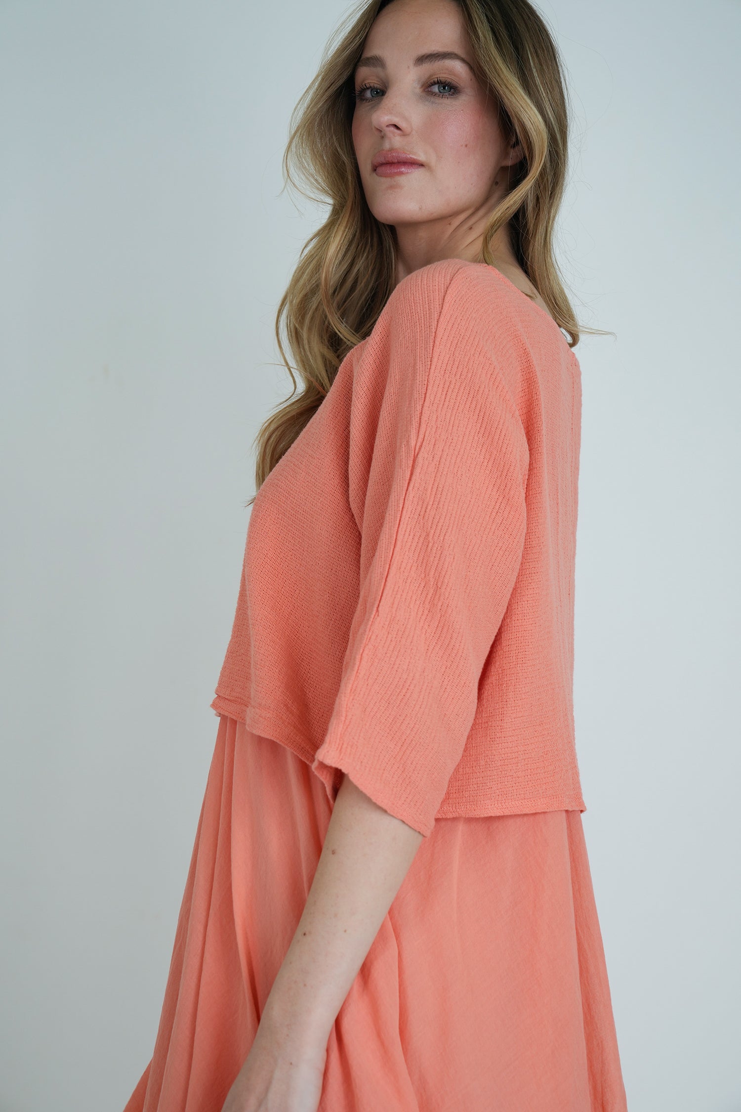 Side view of coral long-sleeve flowy midi dress with soft textured fabric, model posing against a plain backdrop.