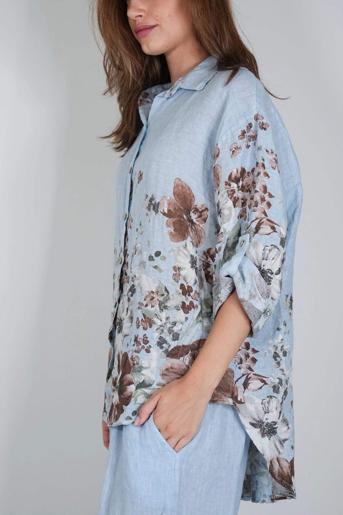 A woman wearing a light blue button-up shirt with a brown and gray floral print, paired with matching light blue pants, shown against a neutral gray background.