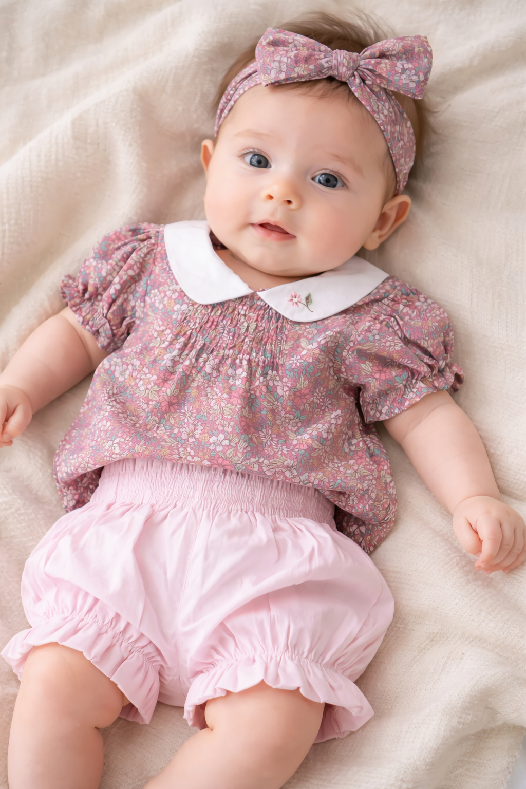 Baby wearing a pink floral outfit with a matching headband on a soft surface