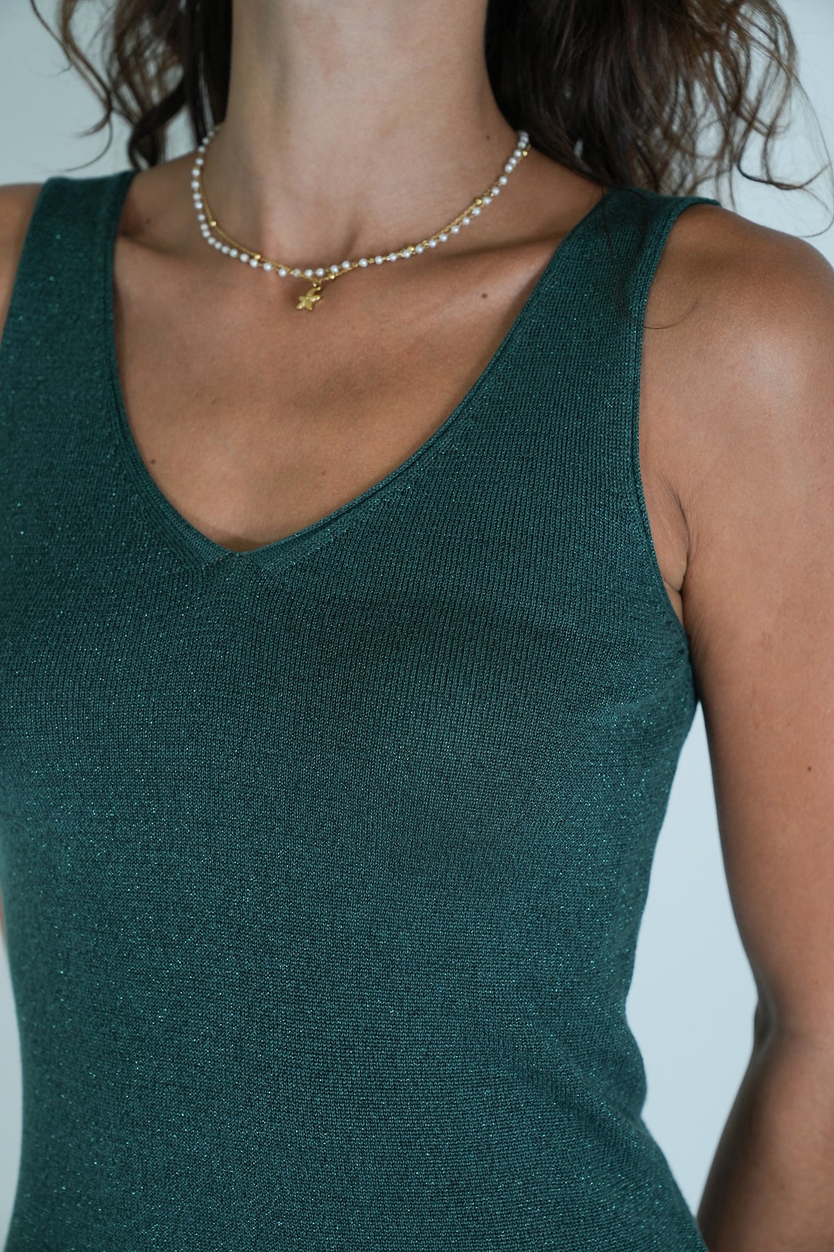 Person wearing a green tank top and pearl necklace with a blurred background