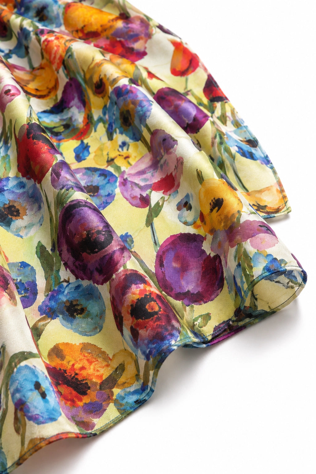 A close-up of a lightweight fabric with a colorful watercolor floral print on a pale yellow background, draped to show its soft texture and folds.