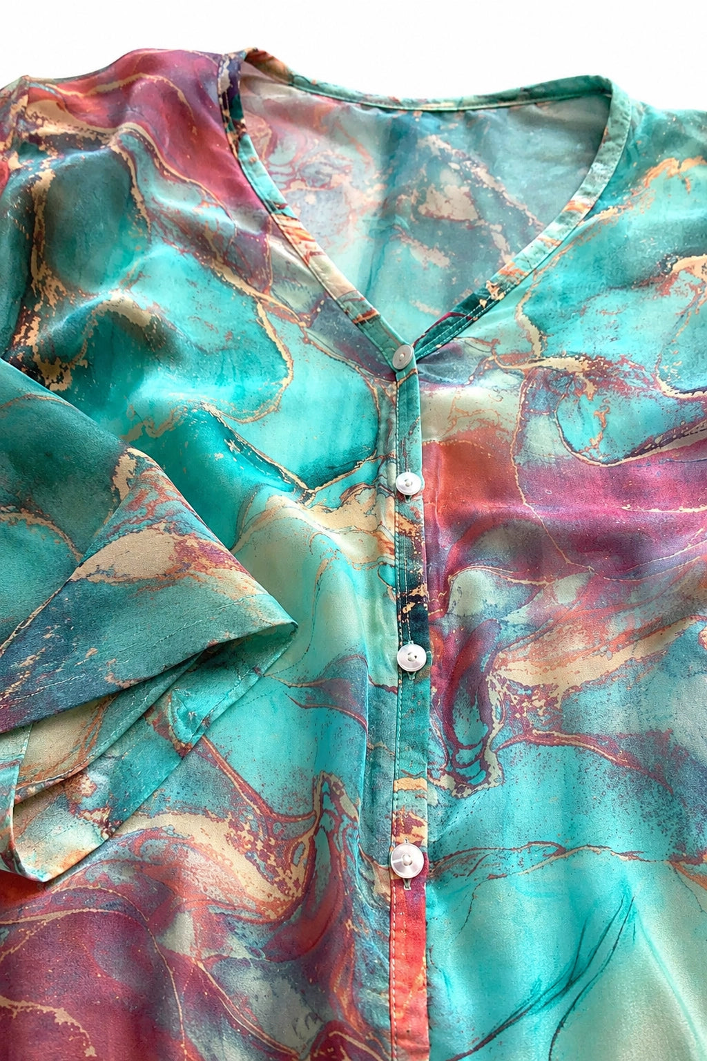 A close-up of a V-neck button-up blouse with a vibrant turquoise, pink, and gold marbled pattern.