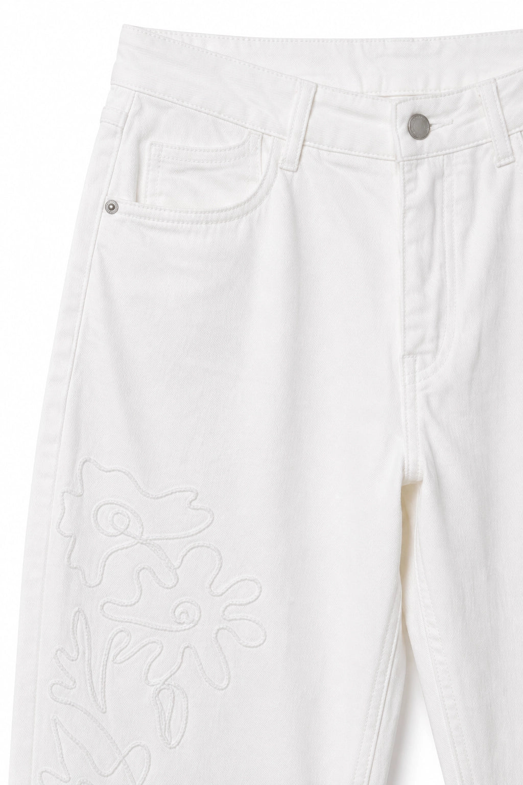 Close-up of white denim jeans showing the front pocket, button waist, and tonal floral embroidery on the lower leg.