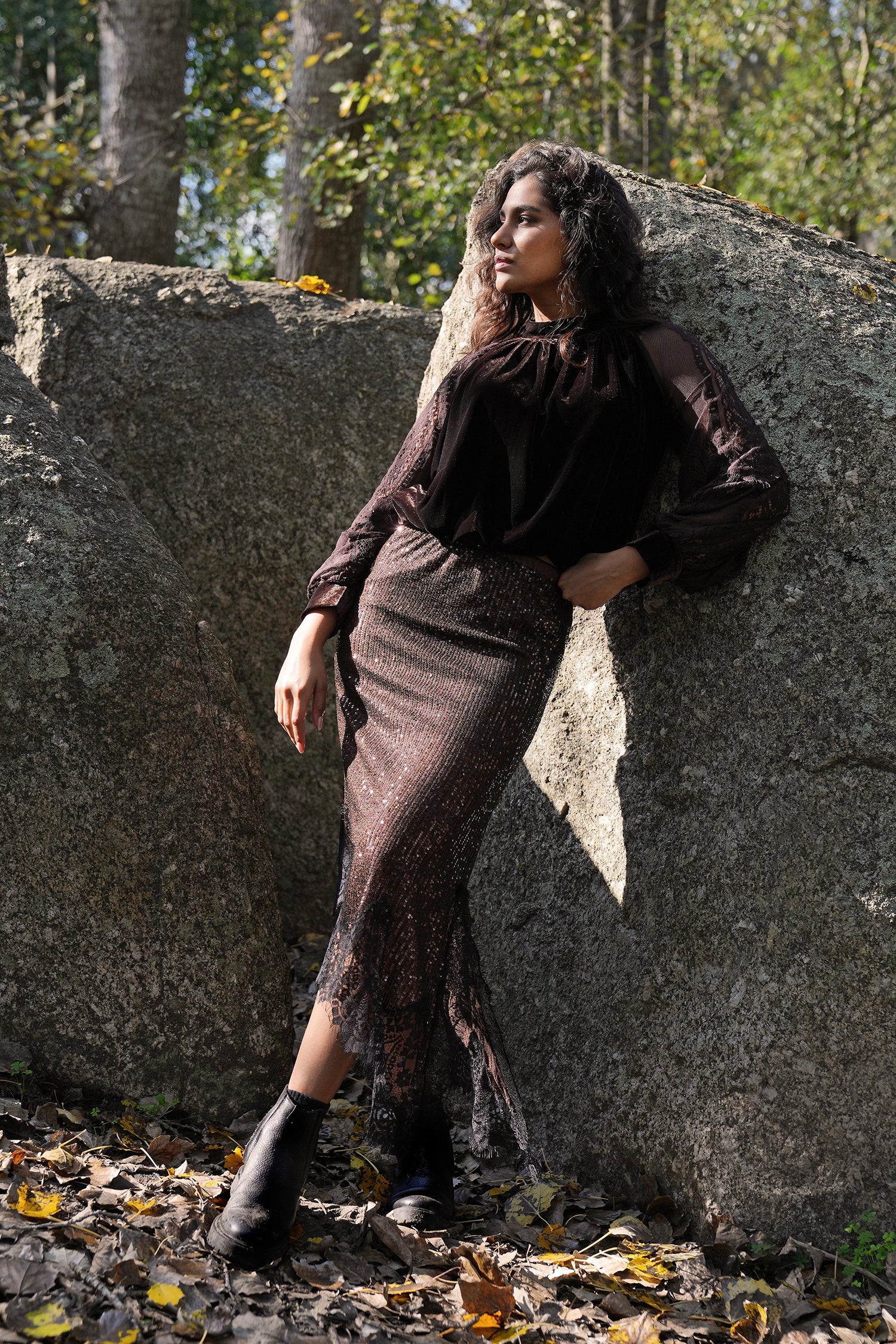 Woman in a dark dress leaning against a large rock with trees in the background