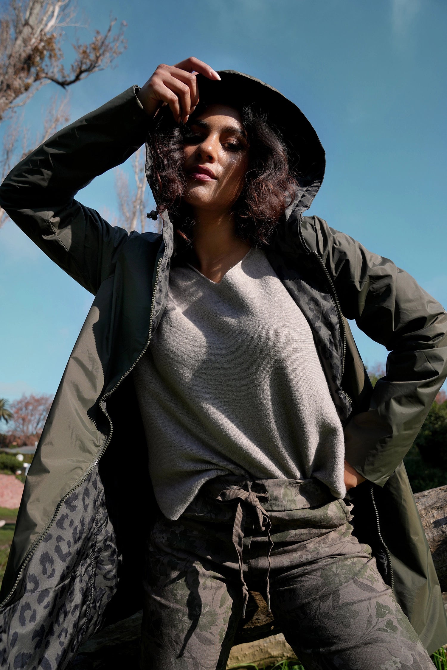 Person wearing a green coat and hat outdoors with a clear blue sky.