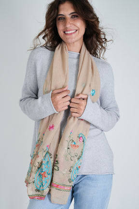 Woman wearing a beige scarf with floral patterns on a plain background
