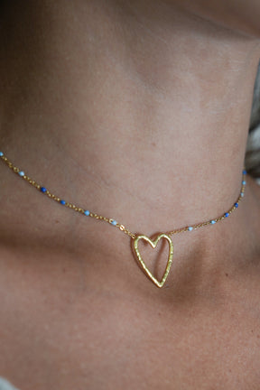 Gold heart-shaped necklace on a person's neck with a neutral background