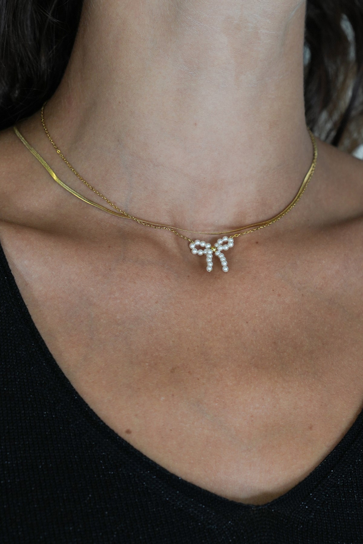 Gold necklace with a bow-shaped pendant on a person's neck