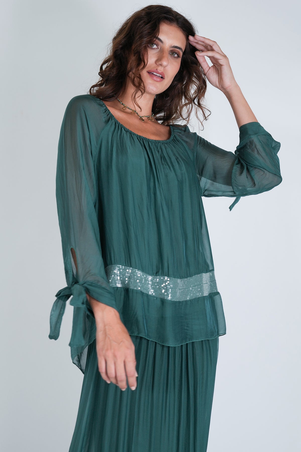 Woman wearing a green top with a sequined waistband on a white background