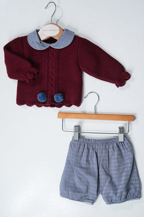 Maroon cardigan with blue collar and shorts on hangers against a white background