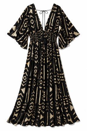 A black maxi dress with a beige geometric tribal pattern, featuring a smocked waist, tie neckline, and wide bell sleeves, shown against a plain white background.