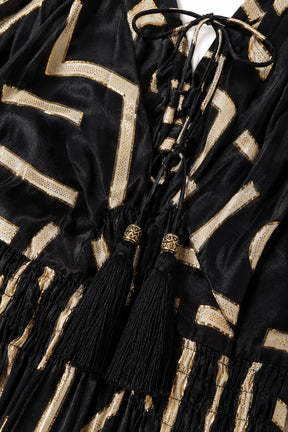Close-up of a black velvet garment with metallic gold geometric stripes and black tassels tied at the neckline.