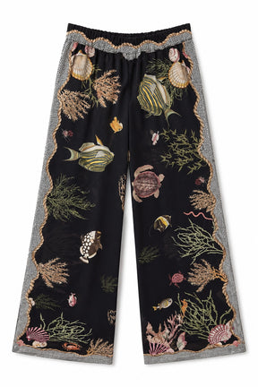 Black wide-leg cropped pants featuring an all-over underwater print of fish, sea plants, and shells, finished with a gray and white patterned scalloped waistband and hem.