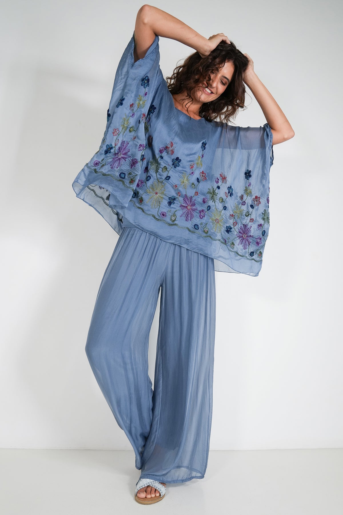 Woman wearing a blue floral top with wide-leg pants against a white background