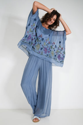 Woman wearing a blue floral top with wide-leg pants against a white background