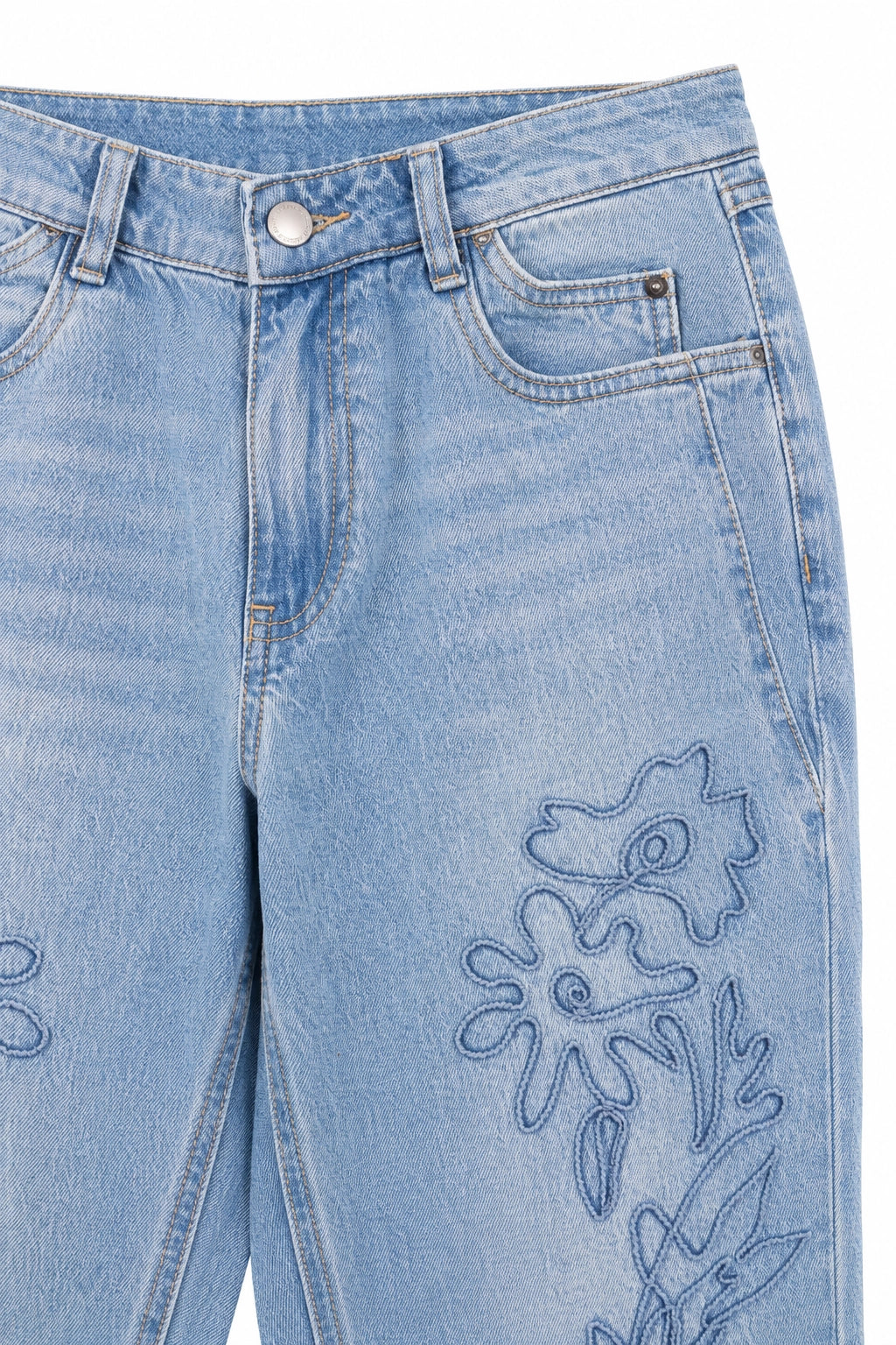 Close-up of light blue denim jeans showing the front waistband, pocket, and floral embroidery on the leg.