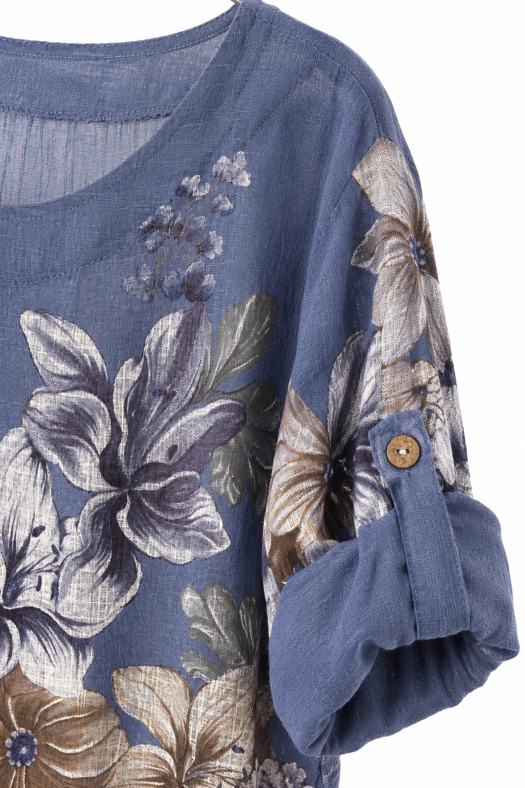 A close-up of a blue floral printed top with a scoop neckline, featuring large lavender, beige, and gray flowers with a rolled-up sleeve showing a wooden button.