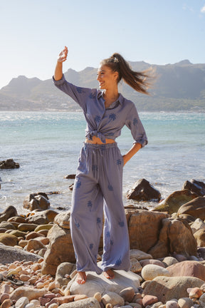 Woman in a light blue outfit standing on a rocky beach with mountains in the background