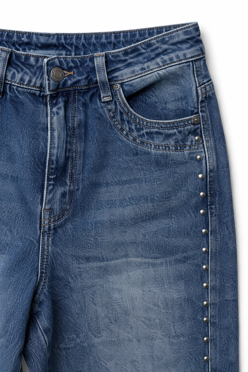 Close-up of blue denim jeans showing the front pocket, button, rivets, and a vertical row of silver studs along the side seam, photographed against a white background.