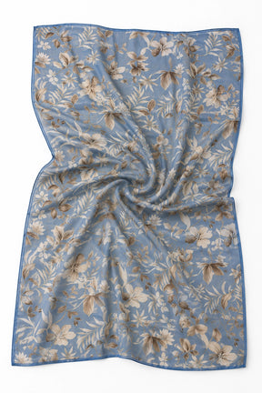 A square scarf with a dusty blue background, featuring an all-over beige and brown floral and leaf pattern, finished with a solid blue border.