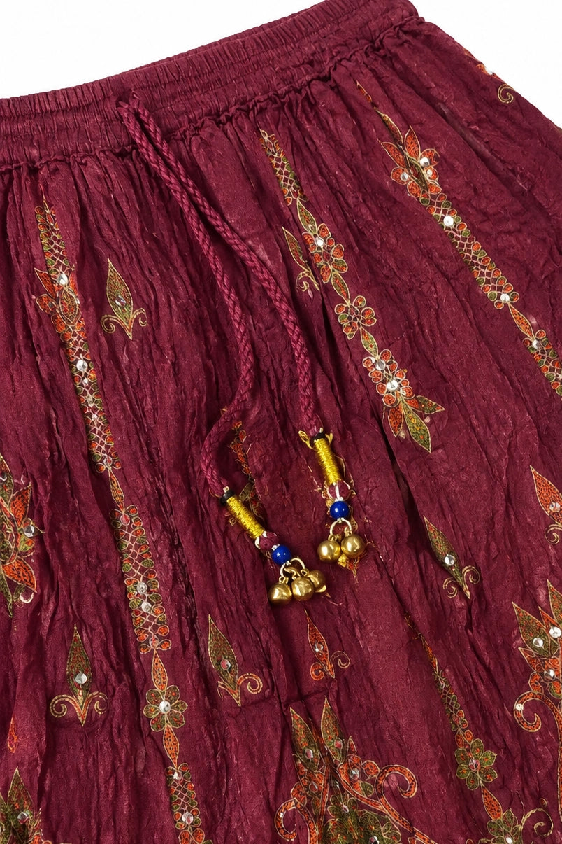 Close-up of a maroon crinkled fabric garment with ornate gold, green, and orange embroidered motifs, sequins, and a braided drawstring with blue and gold beads.