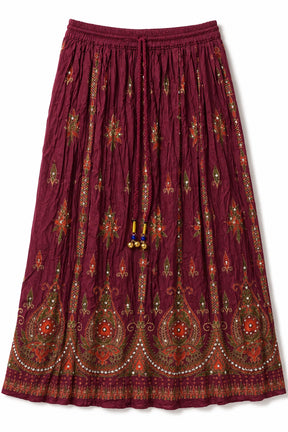 A pleated bohemian-style midi skirt in deep burgundy, decorated with intricate red, green, and gold paisley and floral embroidery and bead tassels.