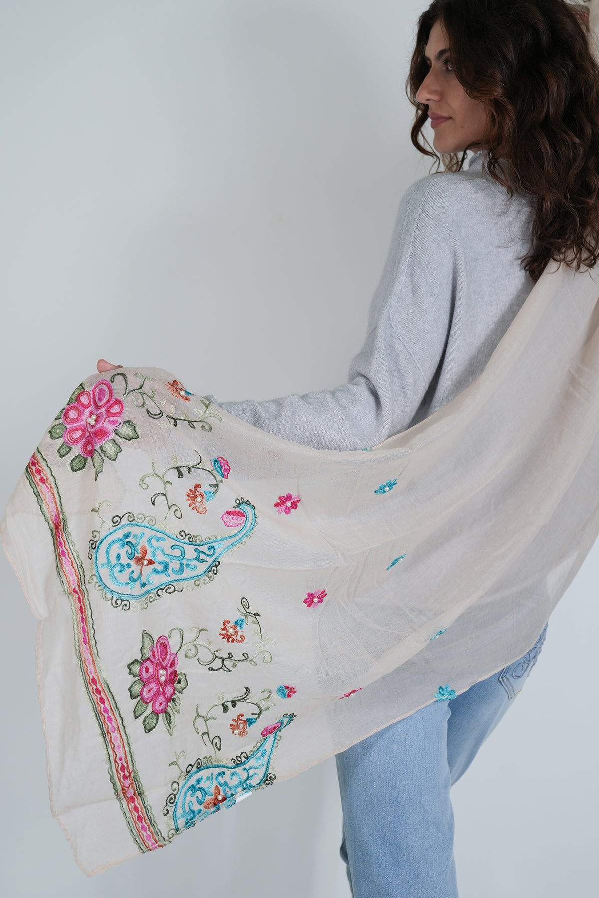 Woman holding a beige embroidered shawl with floral and paisley patterns.