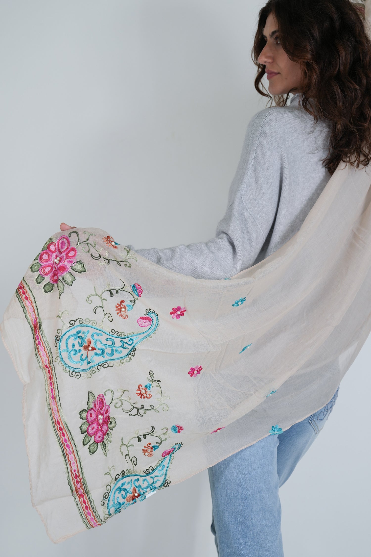 Woman holding a beige embroidered shawl with floral and paisley patterns.