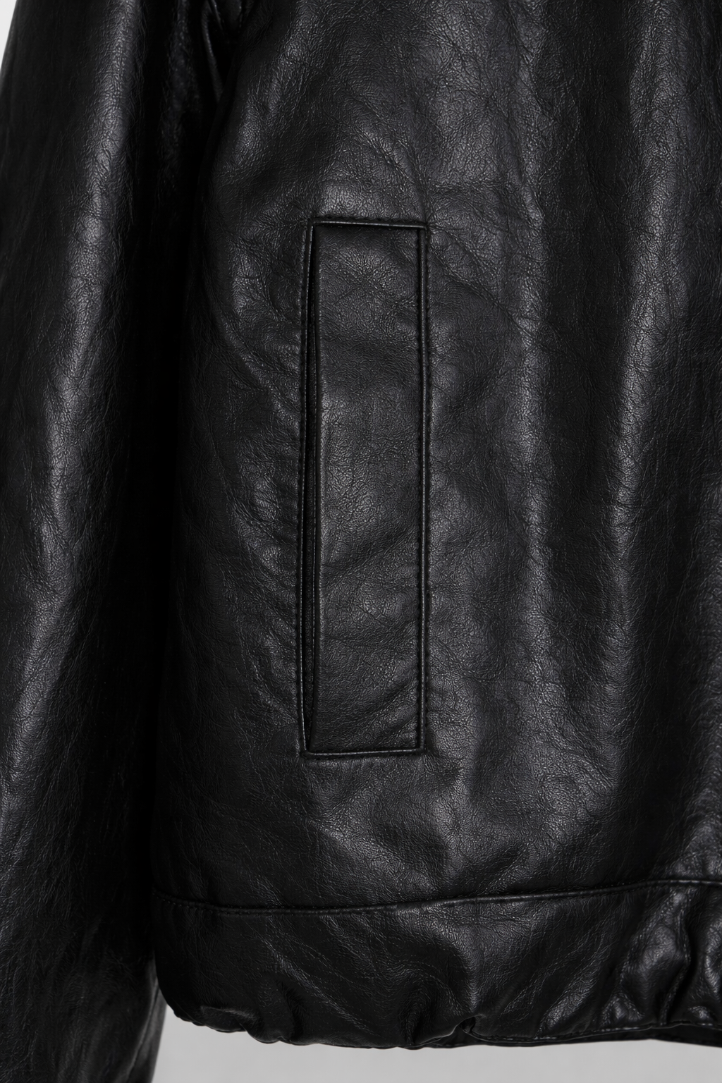 Close-up of a black leather jacket with a pocket detail on a light gray background