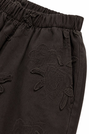 Close-up of dark brown corduroy trousers featuring tonal floral embroidery and an elastic waistband.