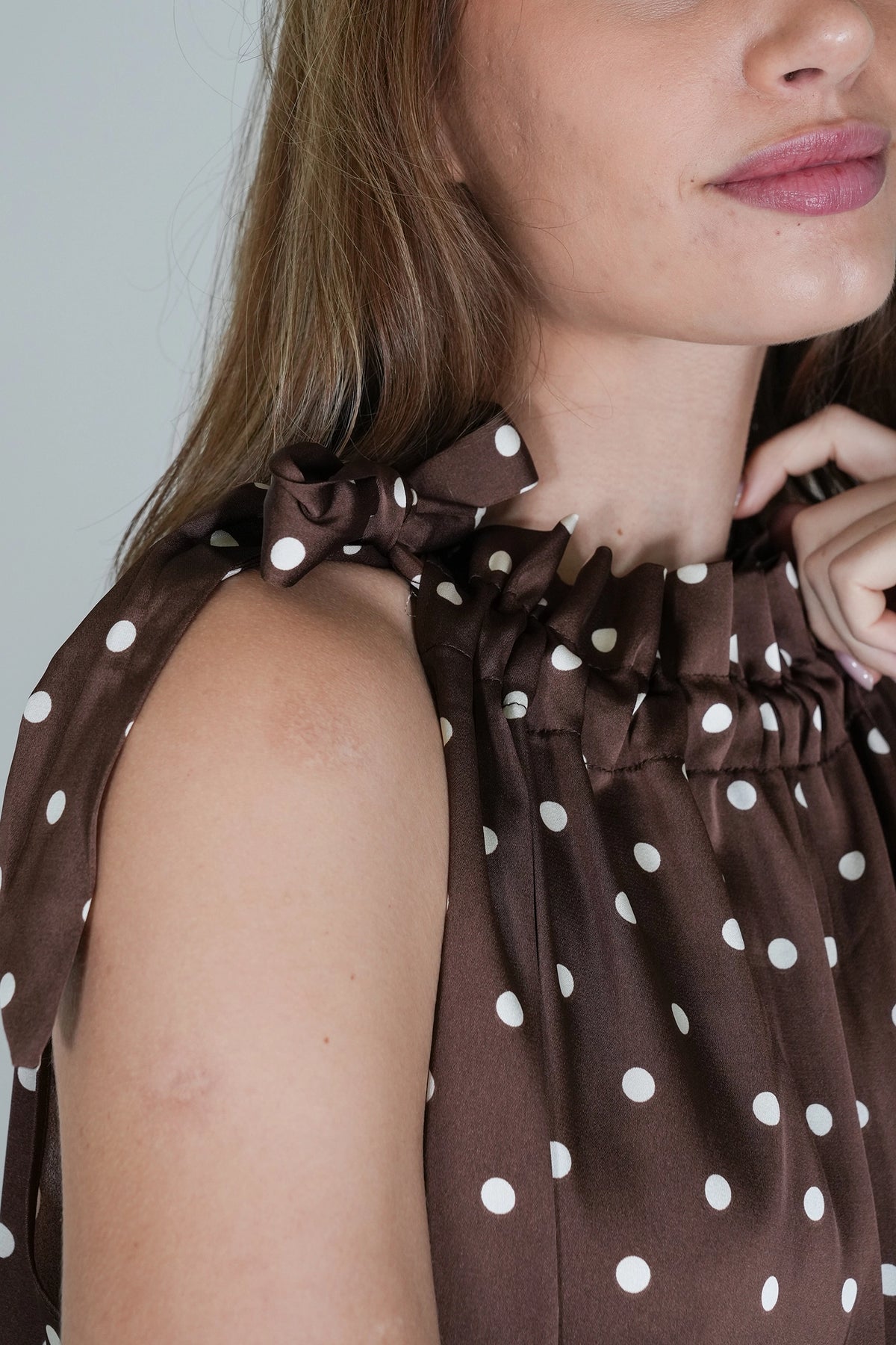 Close-up of a woman wearing a brown sleeveless top with white polka dots and a gathered ruffled neckline.