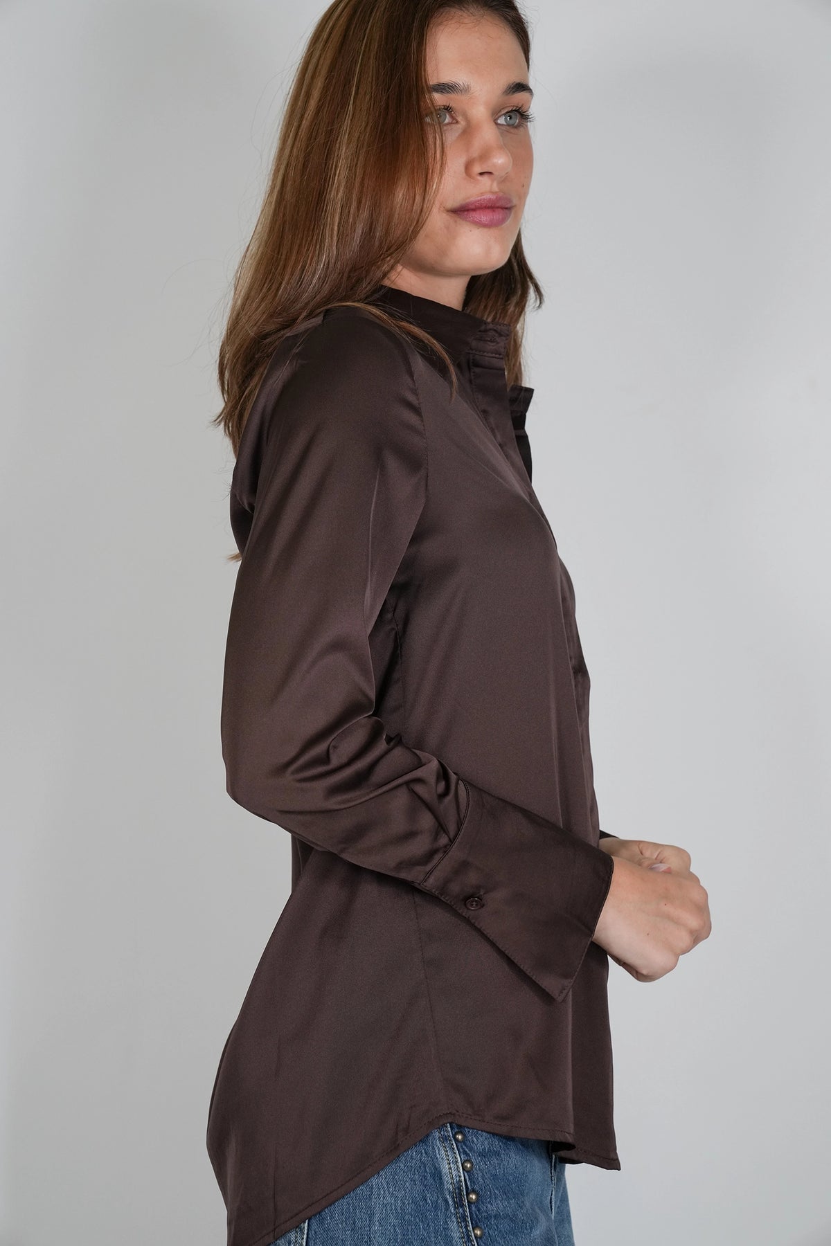 A woman wearing a dark brown long-sleeve hooded top, shown in profile against a plain light gray studio background.