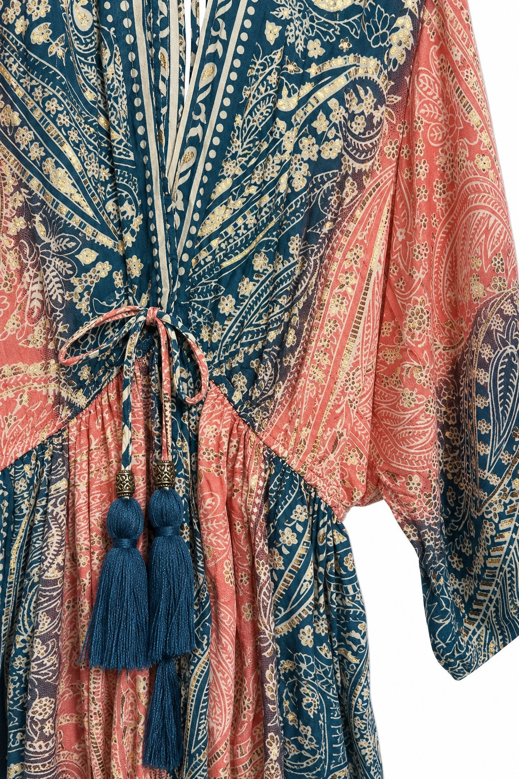 A close-up of a bohemian-style kaftan dress featuring a split design with navy blue and coral pink paisley patterns, cream vertical stripes, and a drawstring waist with blue tassels.