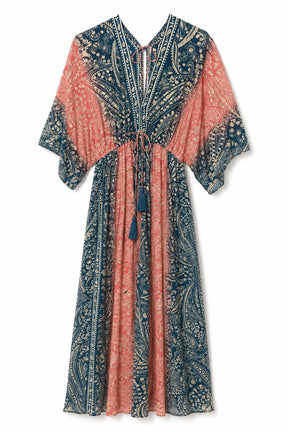 A long, loose kaftan dress with a blue and coral-pink paisley pattern, featuring a split V-neckline, tie waist, and tassel details, shown against a plain white background.