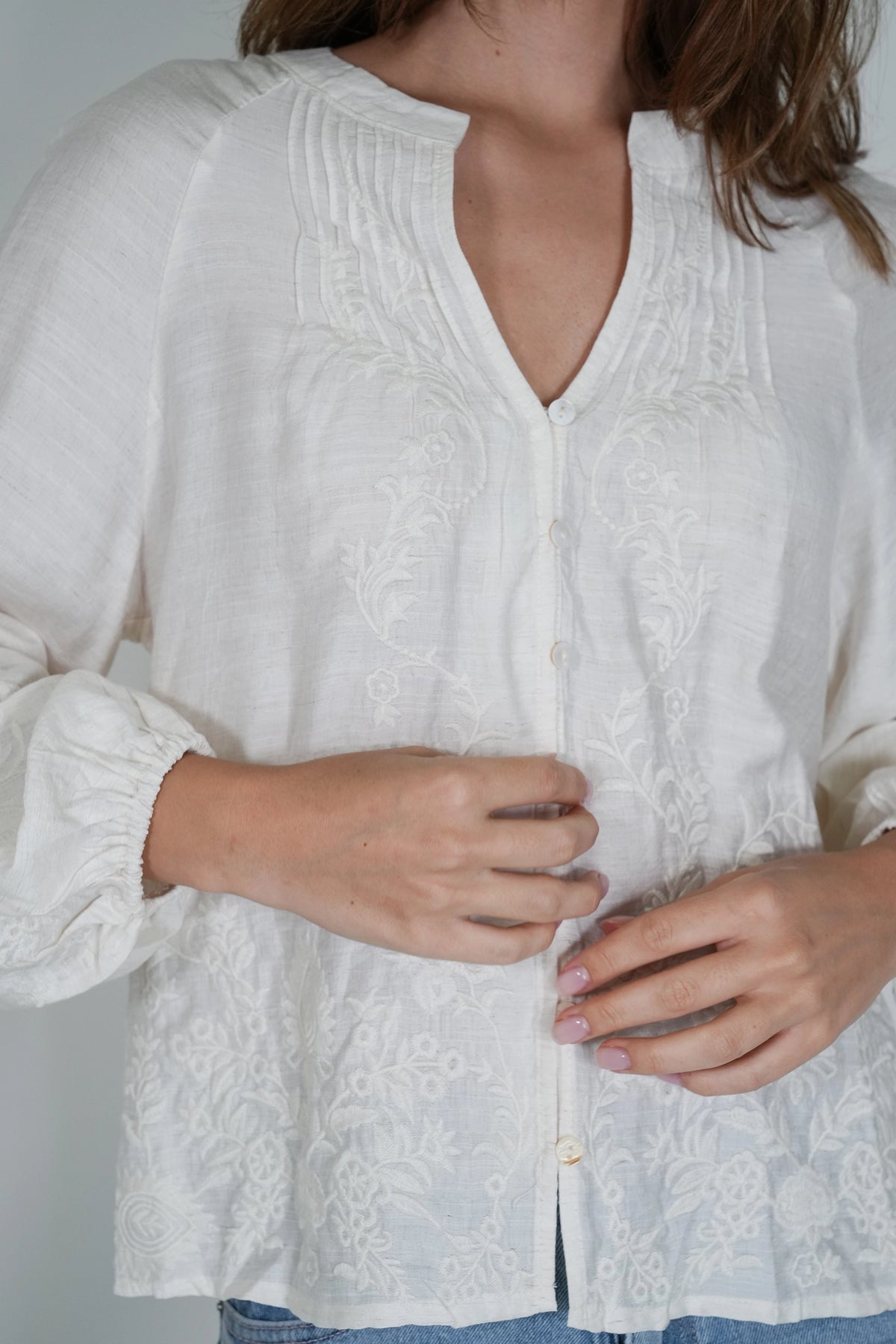 A close-up of a woman wearing a white long-sleeve blouse with delicate floral embroidery and a button-front closure.