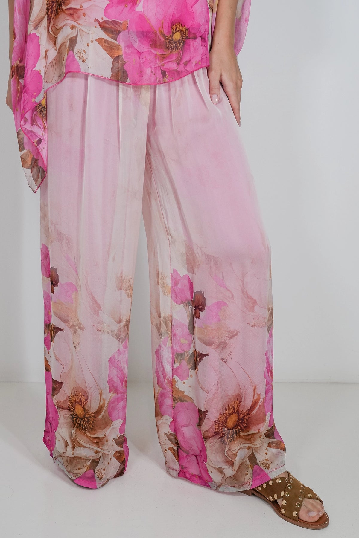 Pink floral wide-leg pants with a sheer mesh fabric, shown on a model wearing brown sandals against a plain white background.