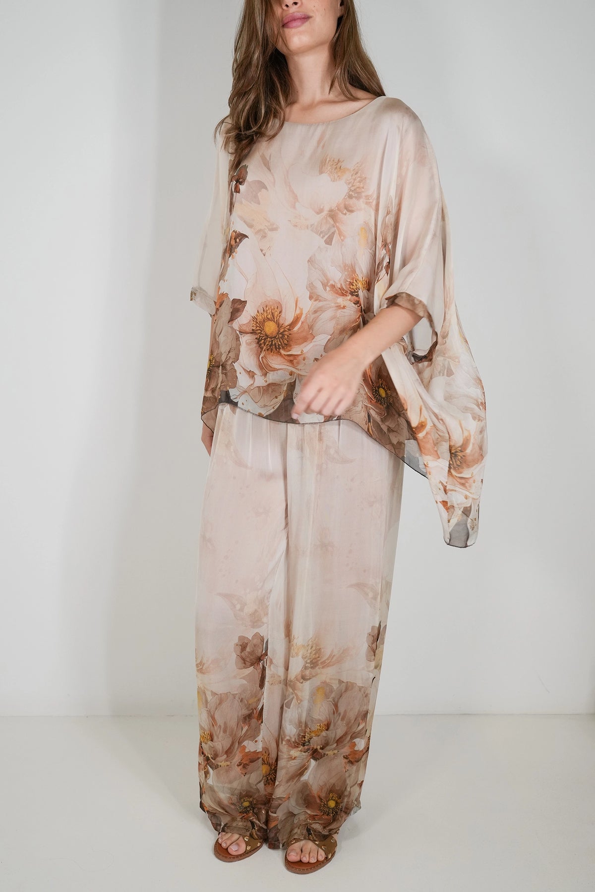 A woman modeling a matching two-piece sheer lounge set with a soft beige and brown floral print, featuring a loose long-sleeve top and wide-leg pants, against a plain white studio background.